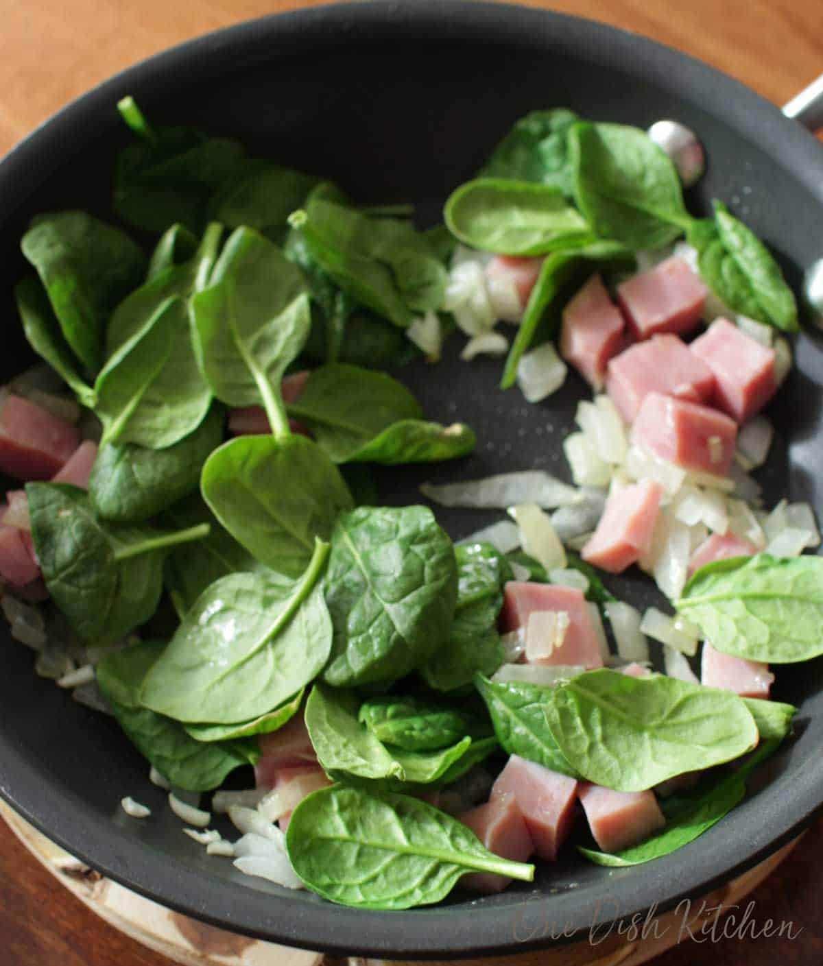 Spinach, onions, and diced ham in a skillet.