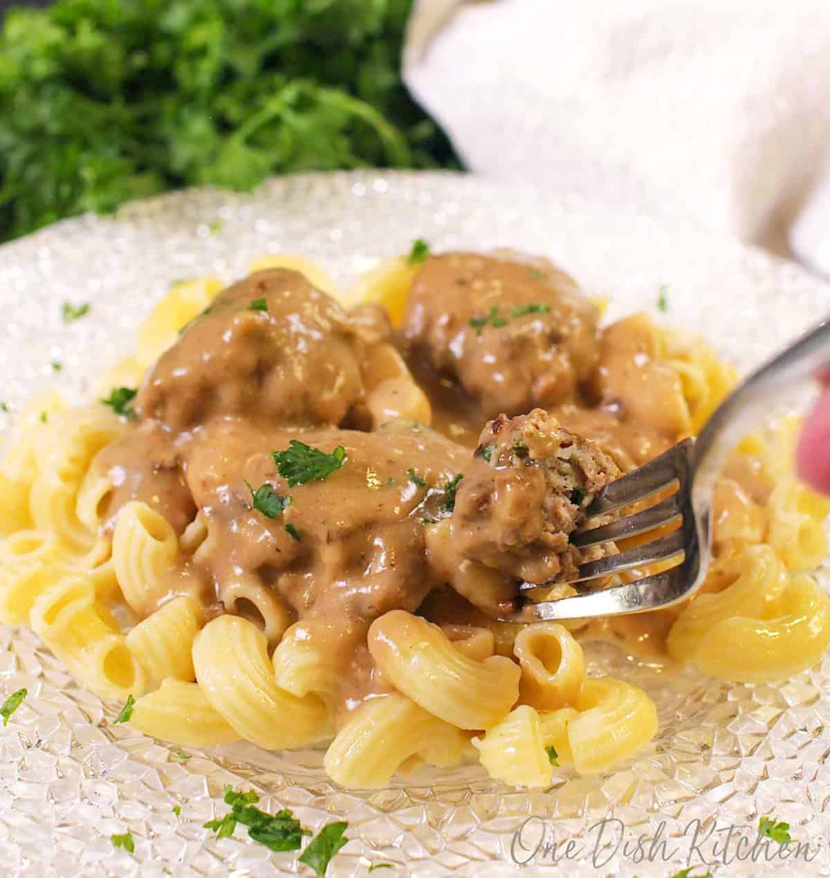 a plate of swedish meatballs over pasta with a fork on the side.