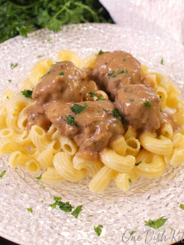 swedish meatballs over noodles on a white plate next to a bunch of parsley