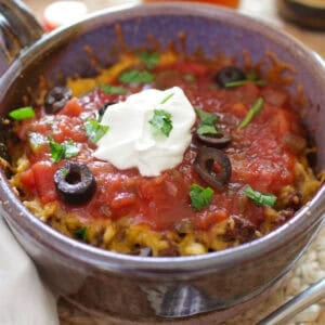 a single serving taco casserole in one baking dish topped with cheese, olives, and sour cream.