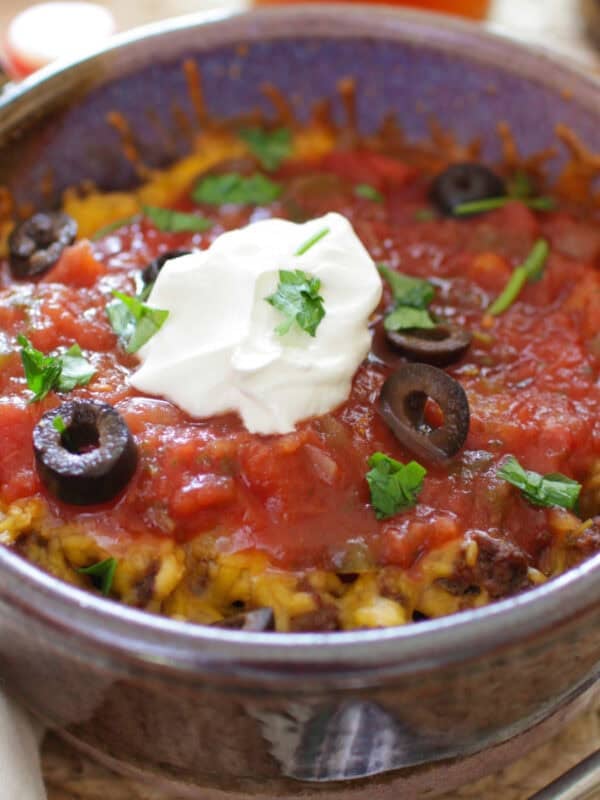 a single serving taco casserole in one baking dish topped with cheese, olives, and sour cream.