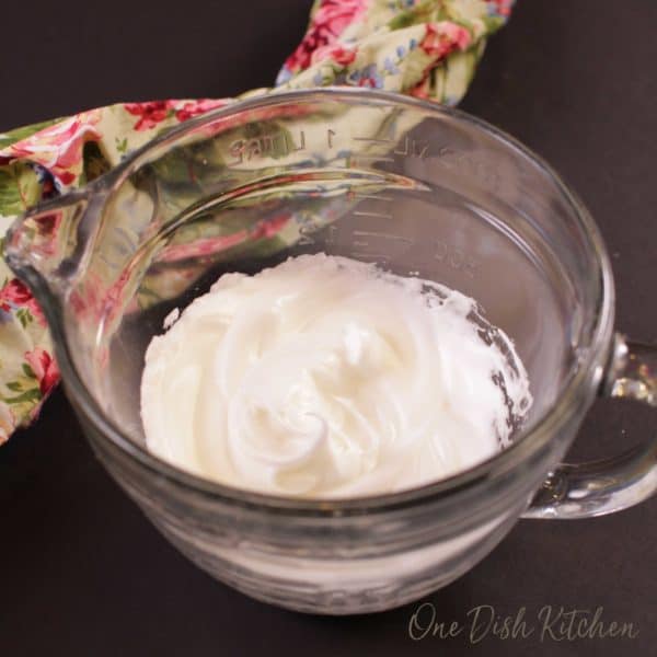 Homemade whipped cream in a large bowl next to a floral cloth napkin