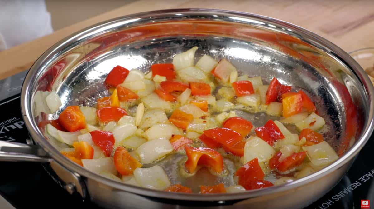 onions, red bell peppers, and garlic simmering in a skillet.