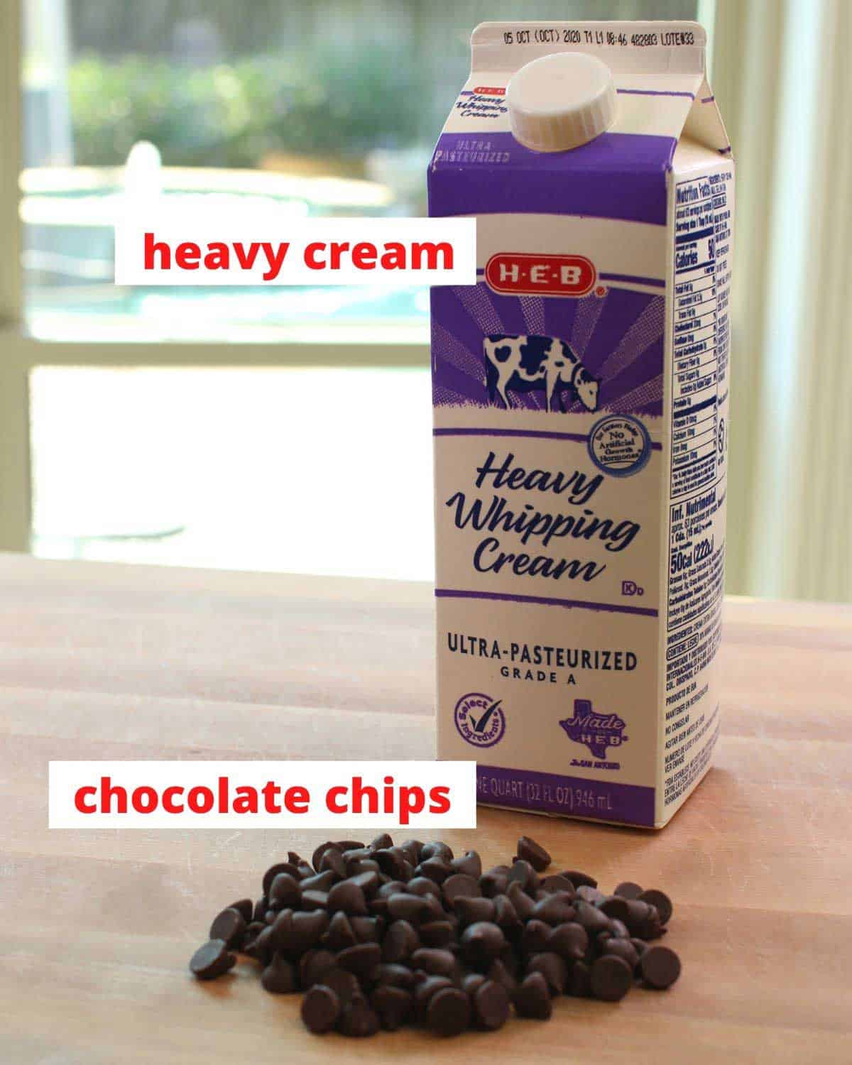 chocolate chips and a carton of heavy cream on a brown cutting board.