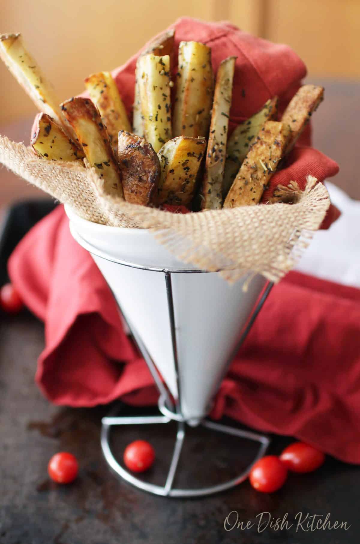 Seasoned french fries in a tall dish held together by a red cloth napkin and a burlap napkin 