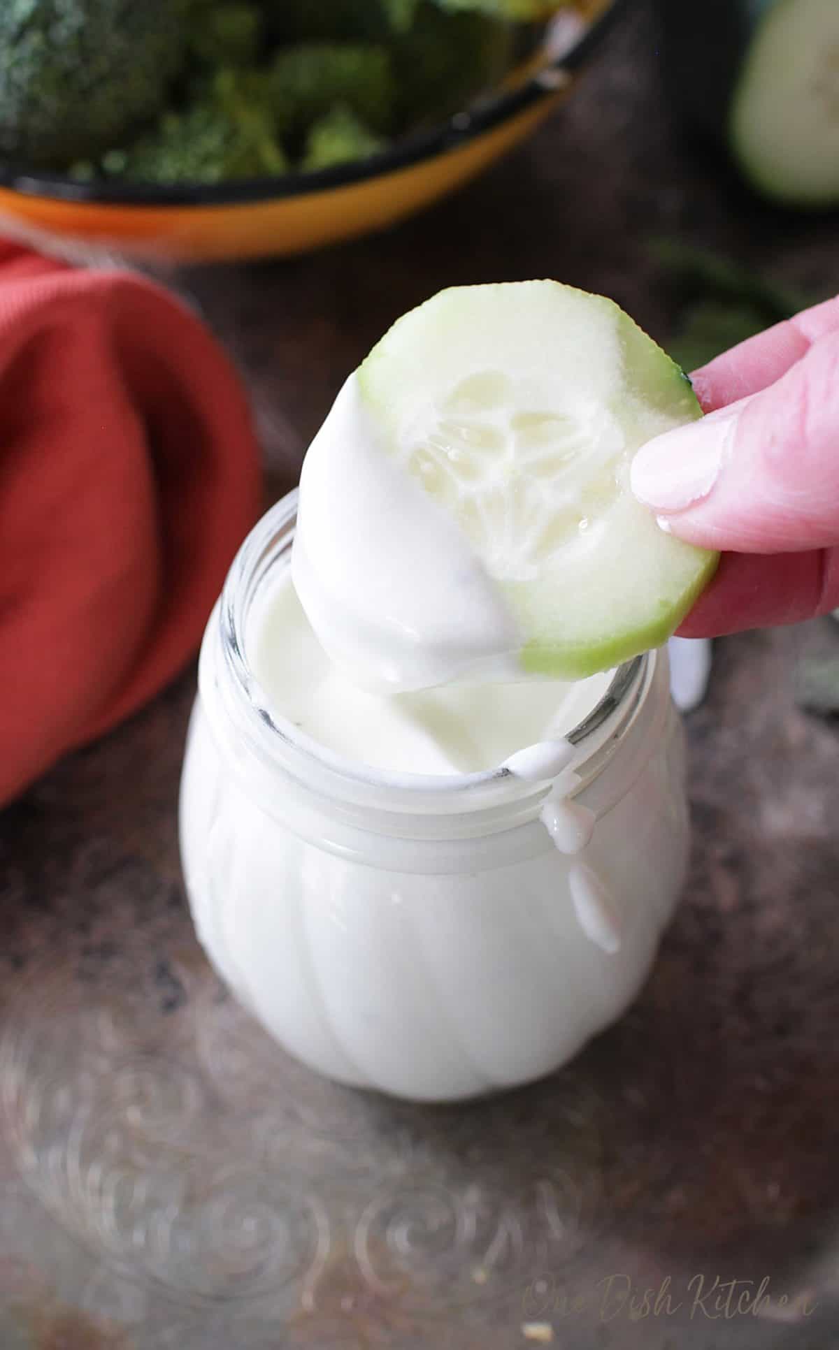 Dipping a cucumber slice in a jar of goat cheese salad dressing.