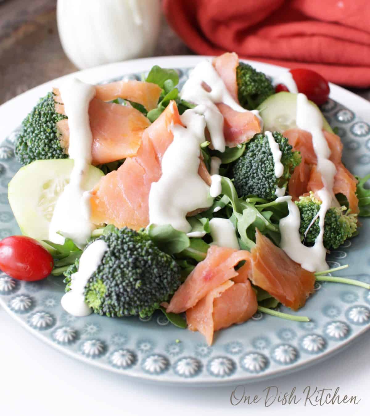 A salad of broccoli florets, smoked salmon, arugula, and cherry tomatoes topped with goat cheese dressing