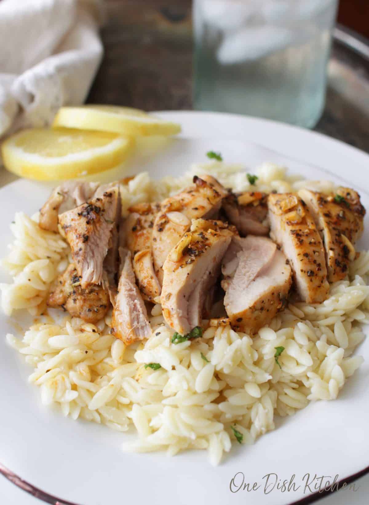 Sliced chicken over orzo pasta on a plate with two lemon wheels 