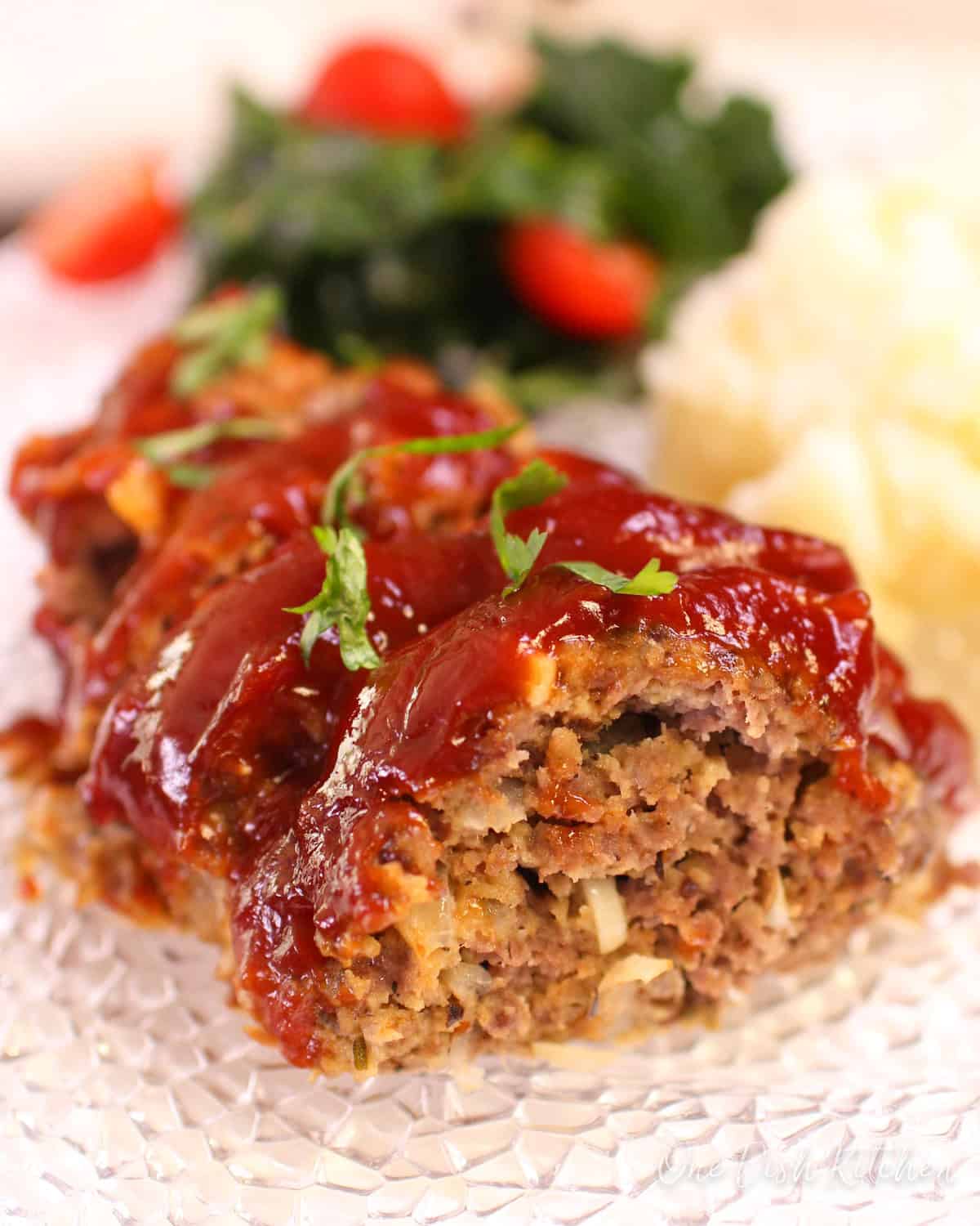 Sliced meatloaf on a plate with mashed potatoes and a small side salad in the background.