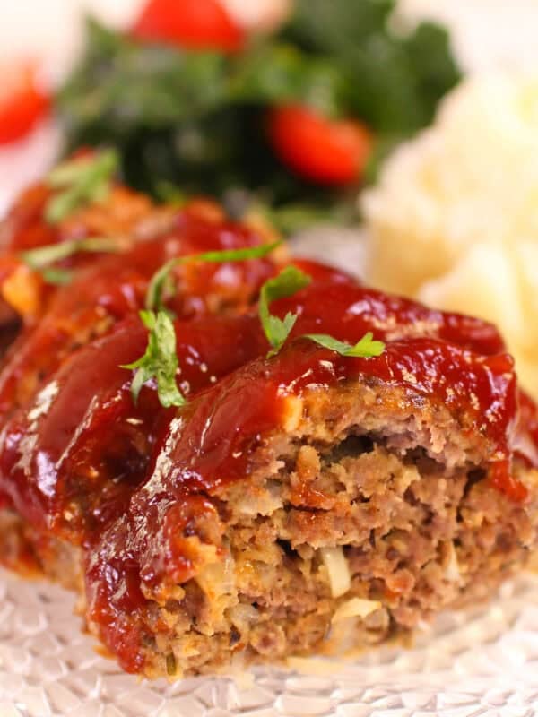 Sliced meatloaf on a plate with mashed potatoes and a small side salad in the background.
