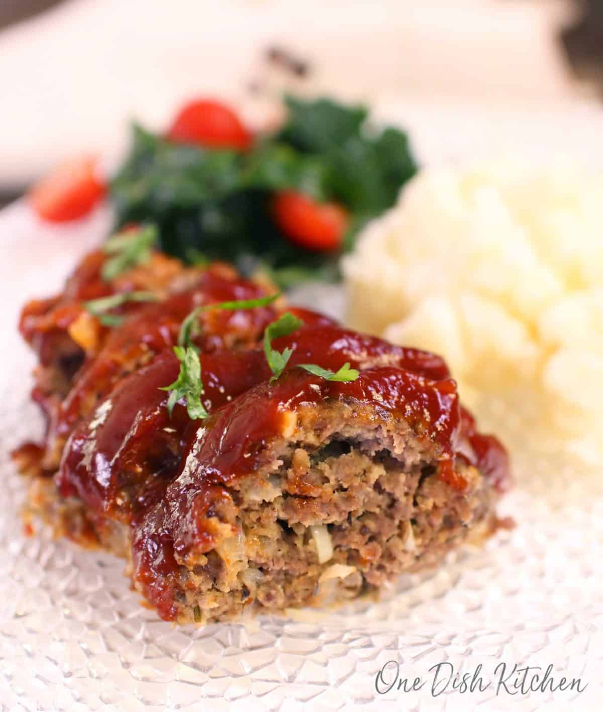 Sliced meatloaf on a plate with mashed potatoes and a small side salad in the background.