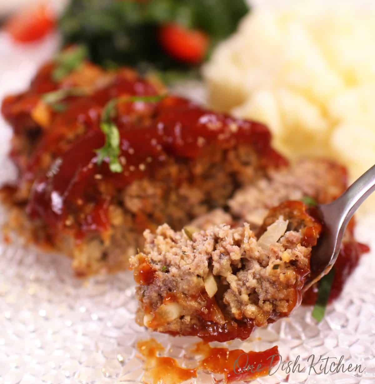 A forkful of meatloaf from a plate with mashed potatoes and a side salad.