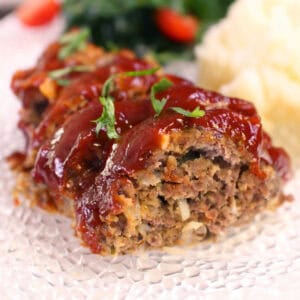 slices of meatloaf on a white plate next to a salad.