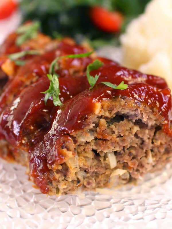 slices of meatloaf on a white plate next to a salad.