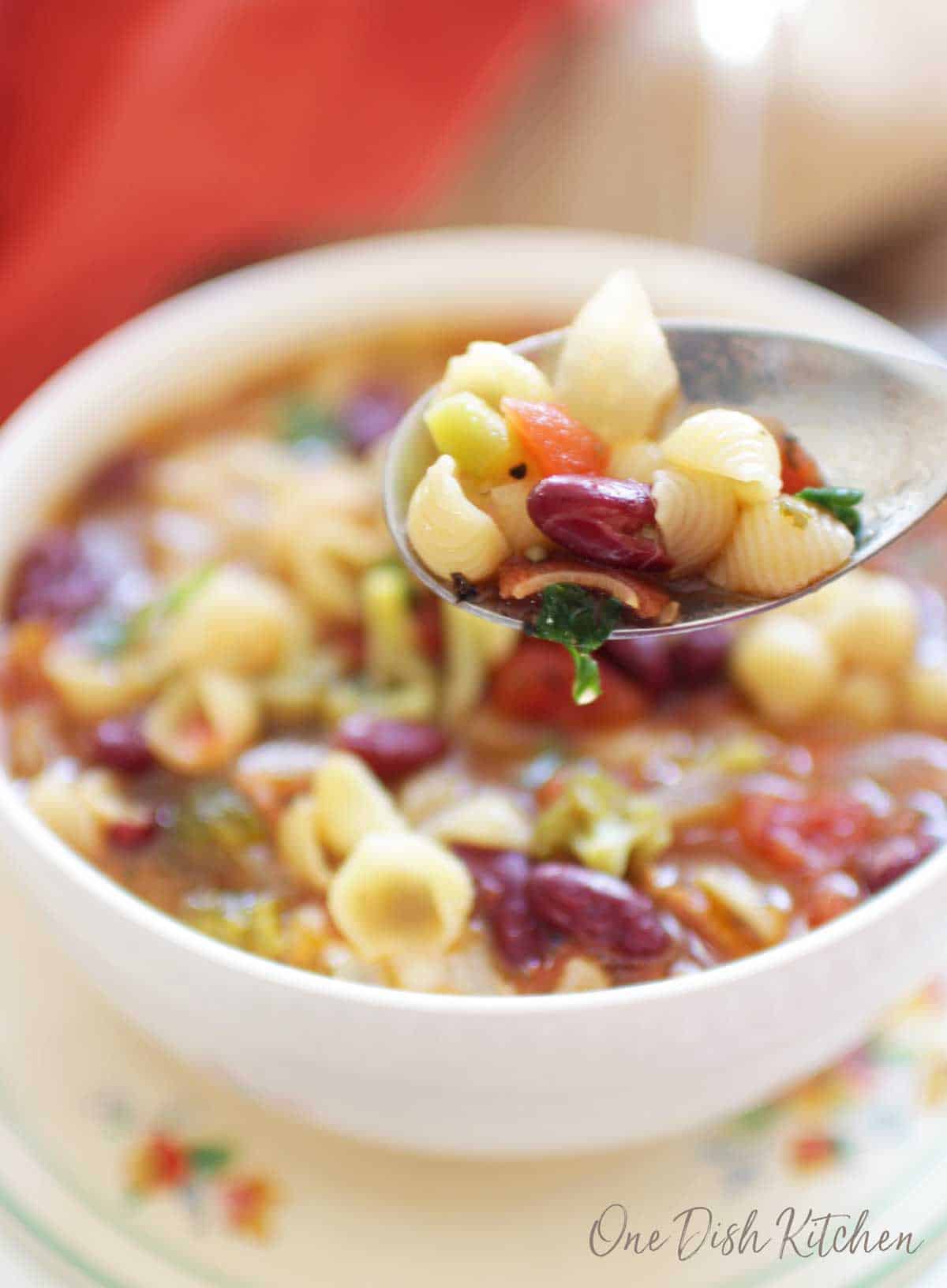 A closeup of a spoonful of minestrone soup filled with beans and pasta noodles.
