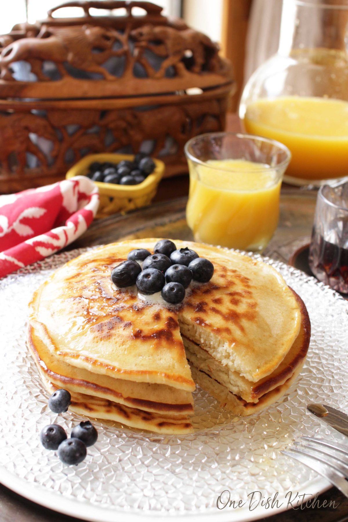 A piece cut out of three pancakes stacked on a plate and topped with melted butter and blueberries.