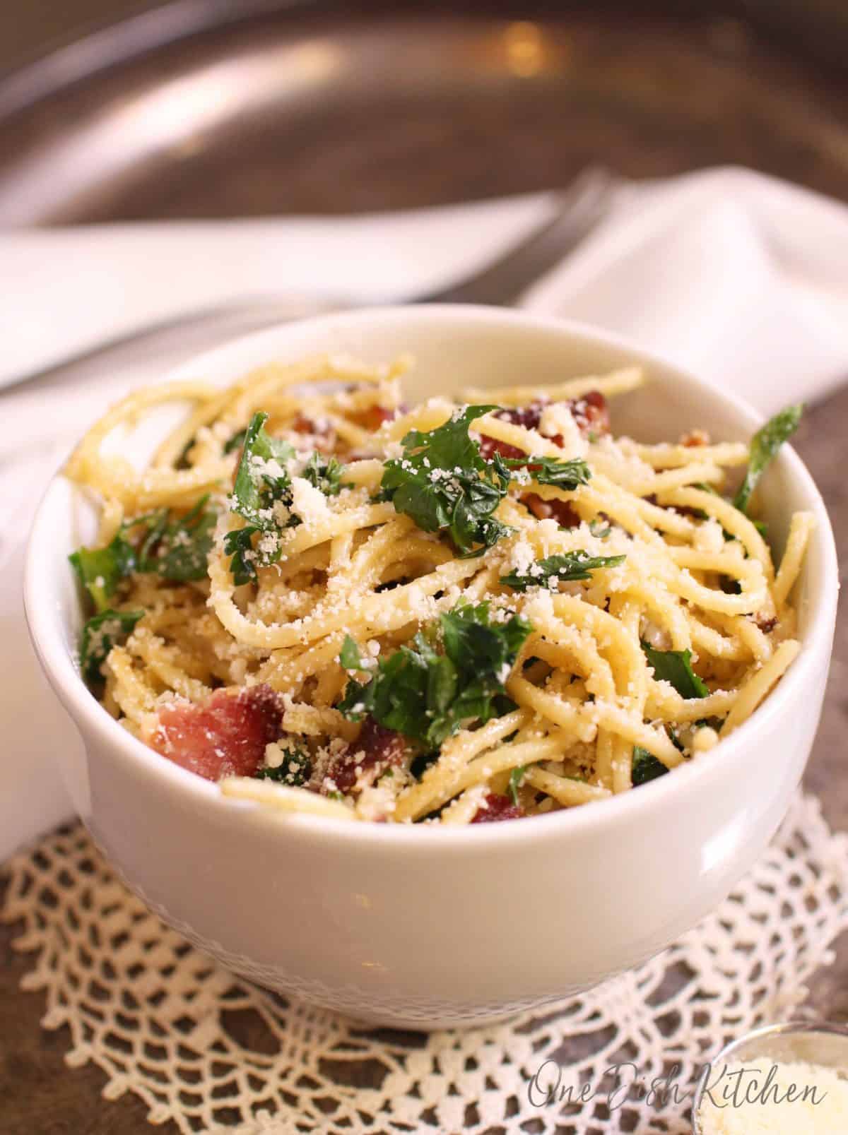 A bowl of pasta carbonara topped with parmesan cheese and parsley on a metal tray.