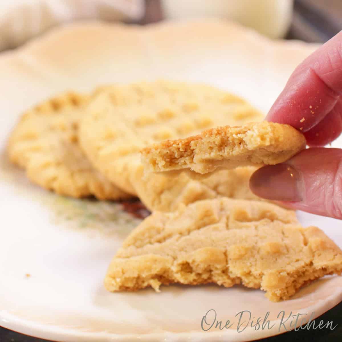 a partially eaten peanut butter cookie on a plate next to a few homemade peanut butter cookies.