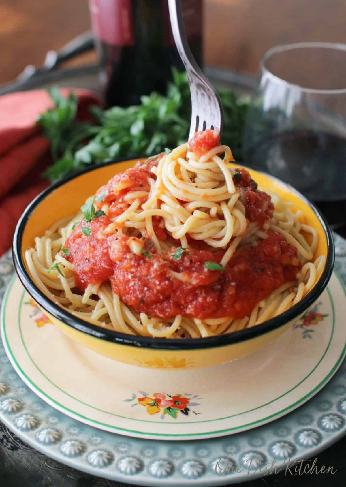 A fork swirling spaghetti that is topped with tomato sauce on a metal tray with a glass of red wine.