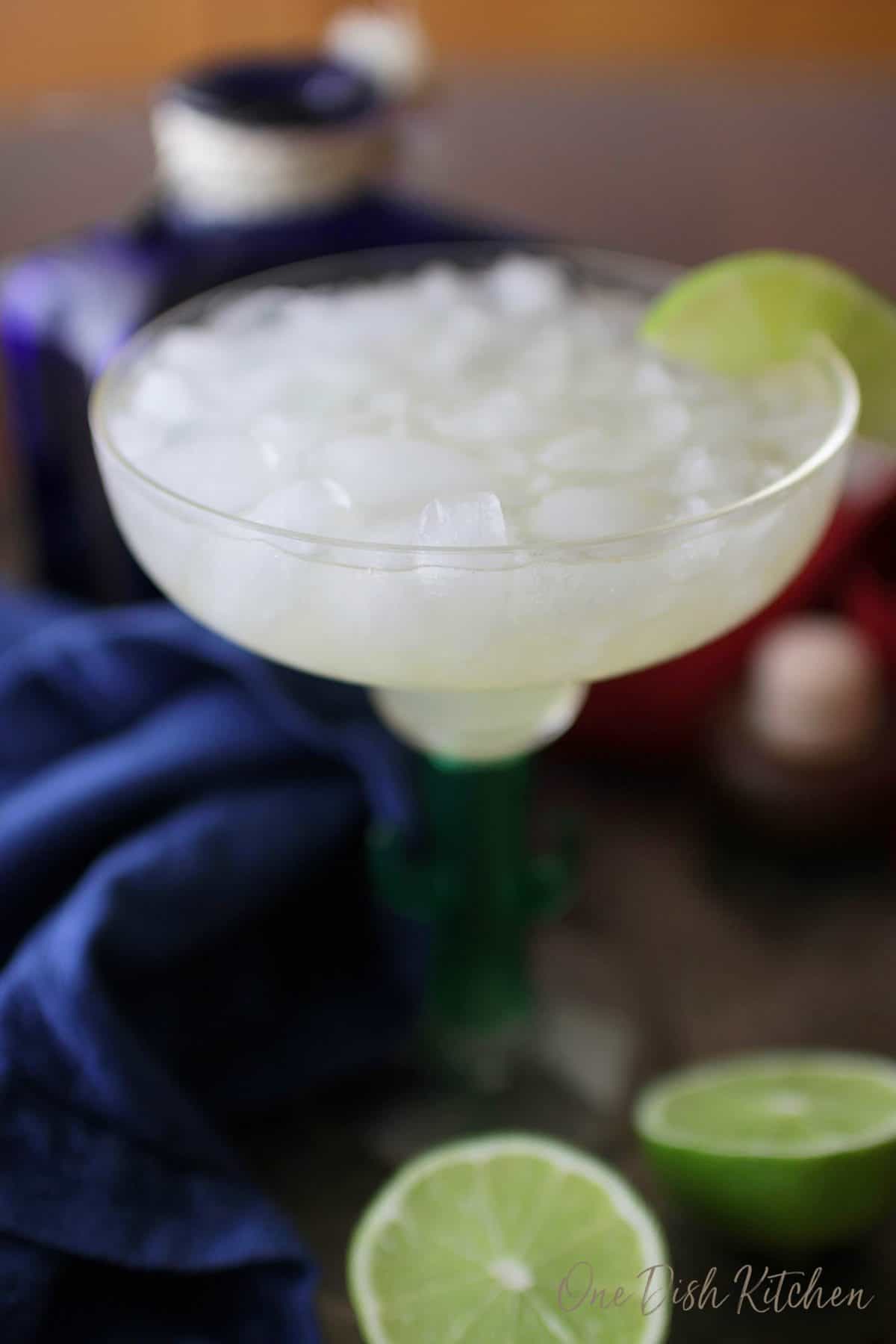 A skinny margarita in a margarita glass garnished with a lime next to two lime halves.