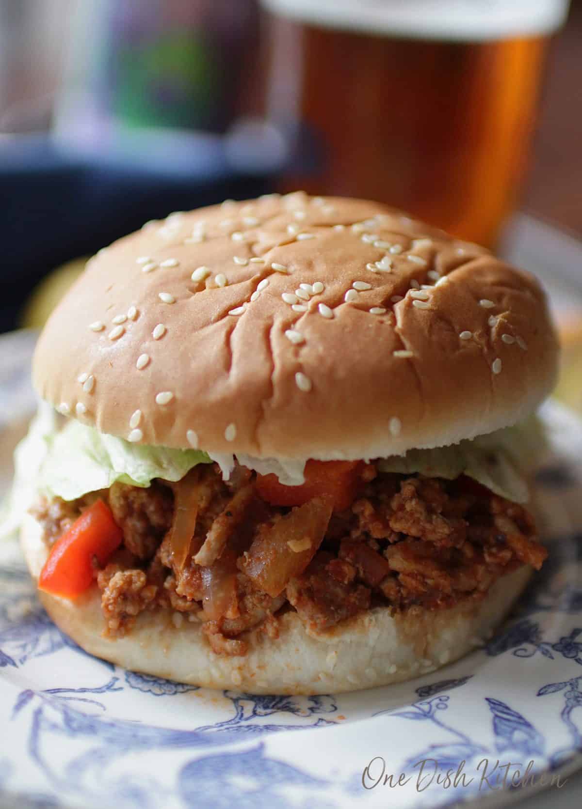 A sloppy joe with lettuce and tomato between a hamburger bun with sesame seeds on a plate