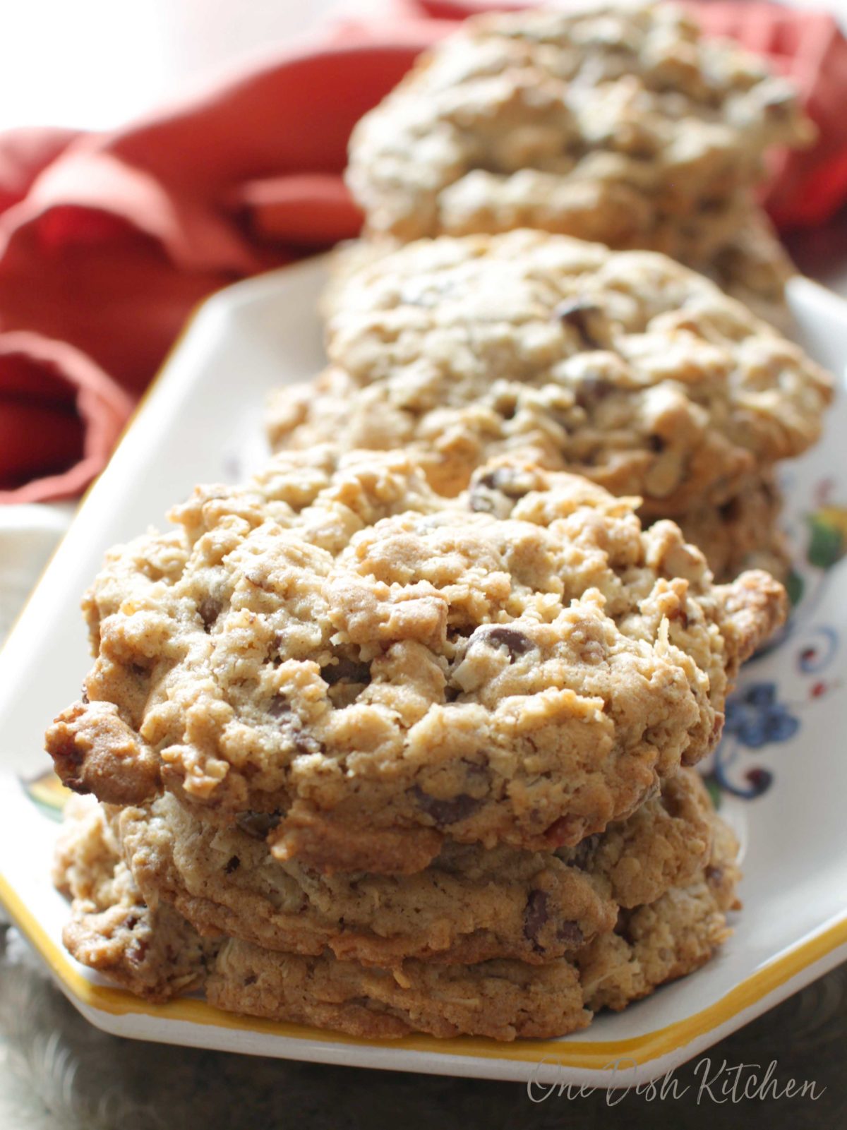 A stack of cowboy cookies on a plate next to an orange napkin.