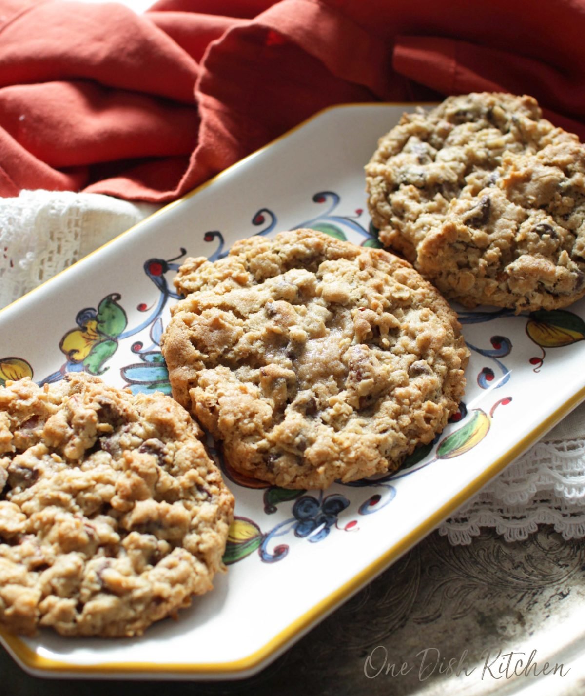 Three cowboy cookies on a plate next to an orange cloth napkin.