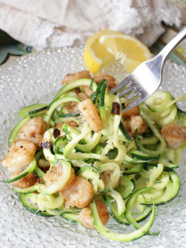 zucchini noodles on a plate with shrimp mixed in and a fork placed on the side of the plate