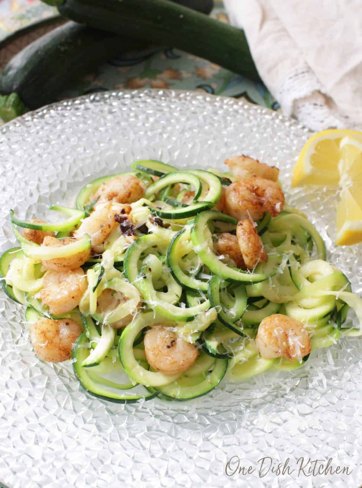 Zucchini noodles topped with grilled shrimp and parmesan cheese on a plate with lemon slices