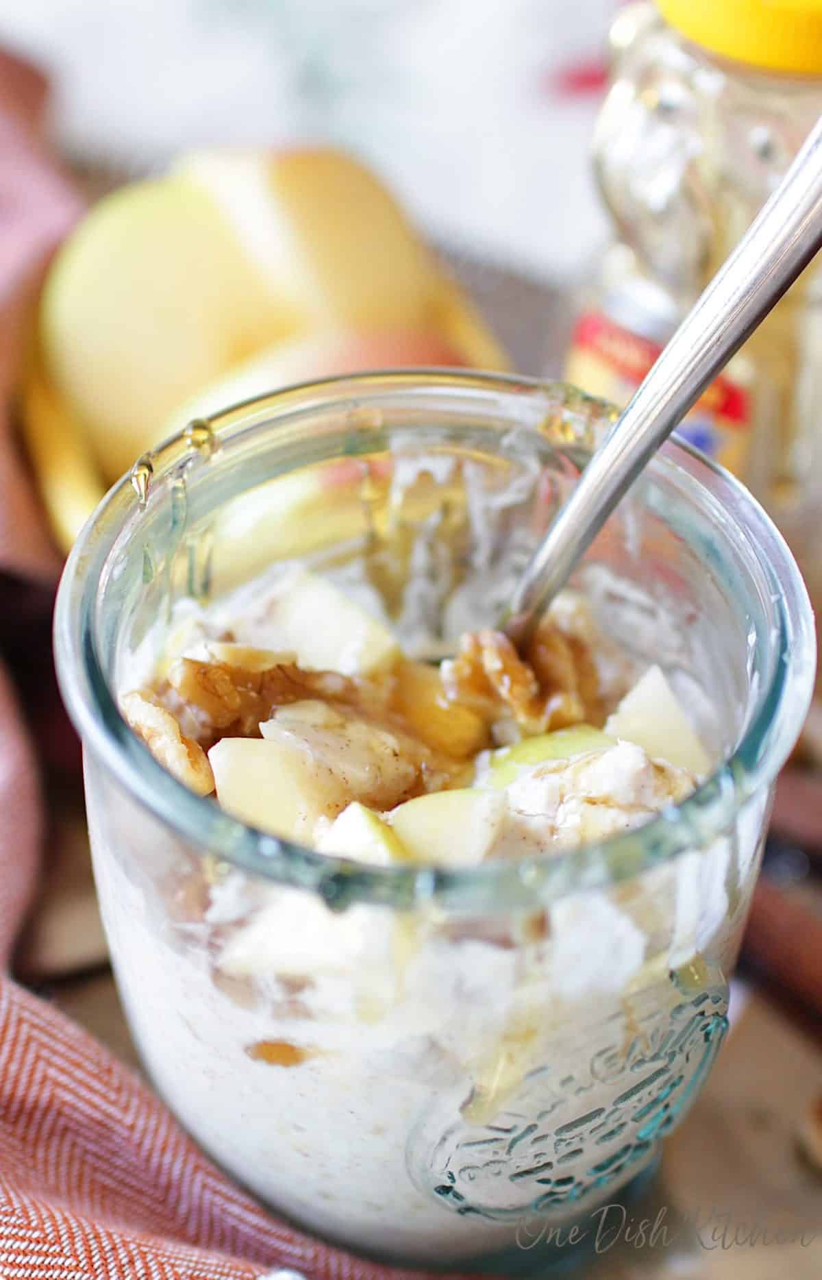 A closeup picture of a jar of overnight oats with a spoon and honey drizzled over the top.