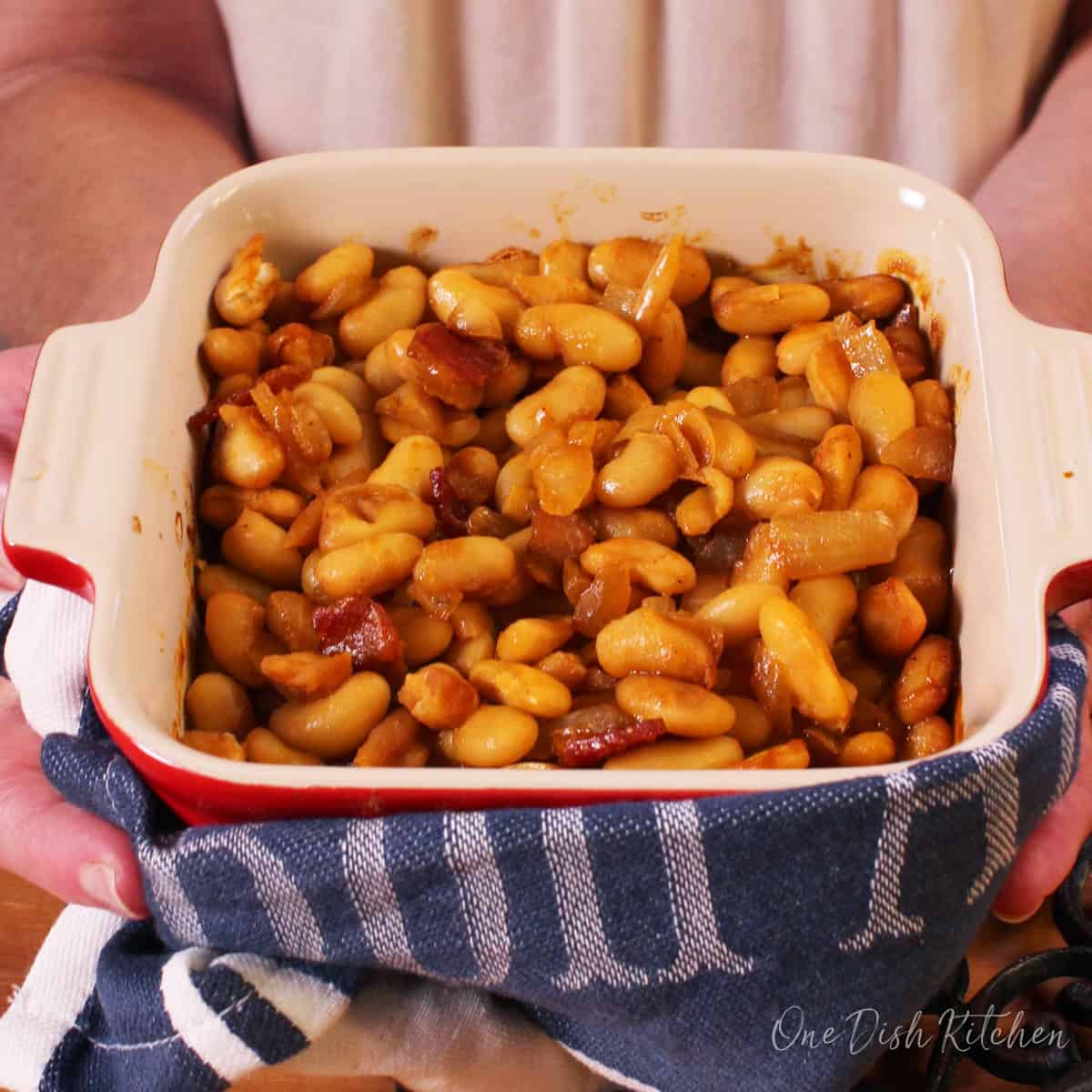 a small batch of baked beans in a red baking dish surrounded by a blue towel.