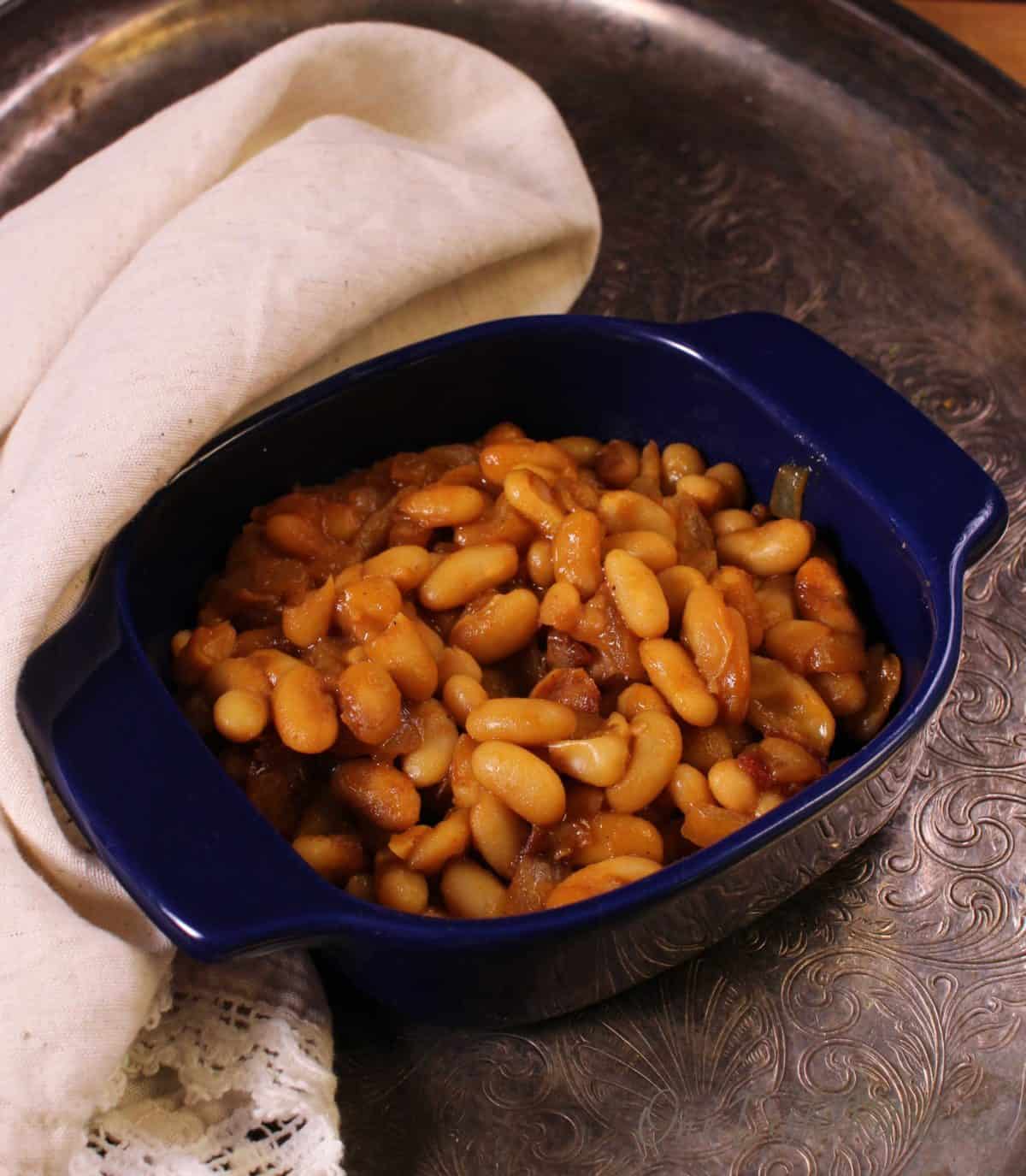Baked beans in a small baking dish on a metal tray with a cream-colored cloth napkin