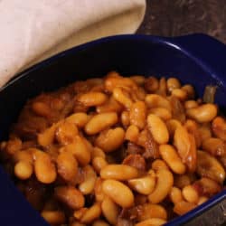 a blue bowl filled with baked beans with bits of cooked bacon on top.