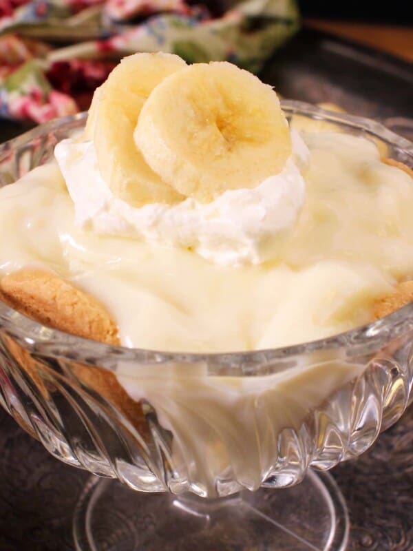 a small banana cream pie in a dessert dish next to a floral napkin