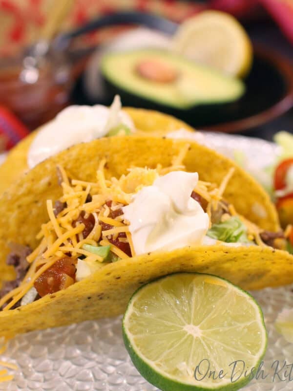 two beef tacos topped with sour cream, and cheese.
