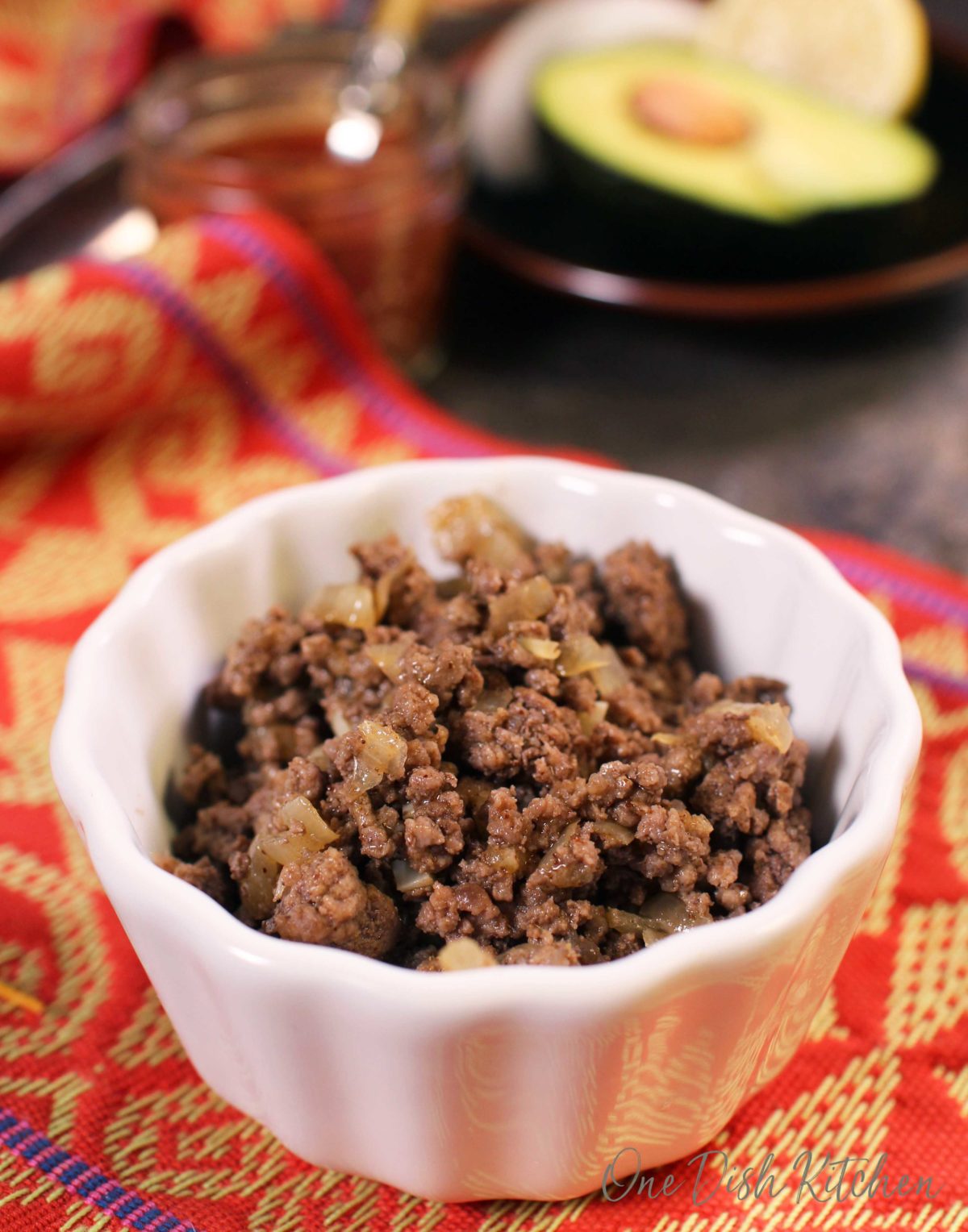 A closeup of a small bowl of ground beef and cooked onions with half of an avocado in the background.