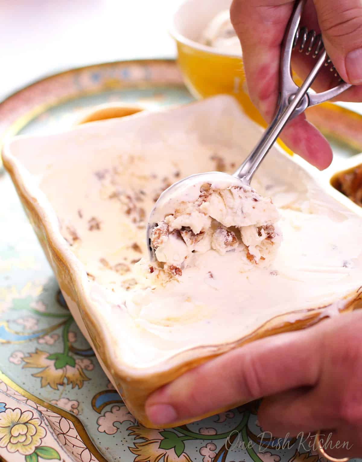a glass dish holding homemade butter pecan ice cream next to an ice cream scoop.