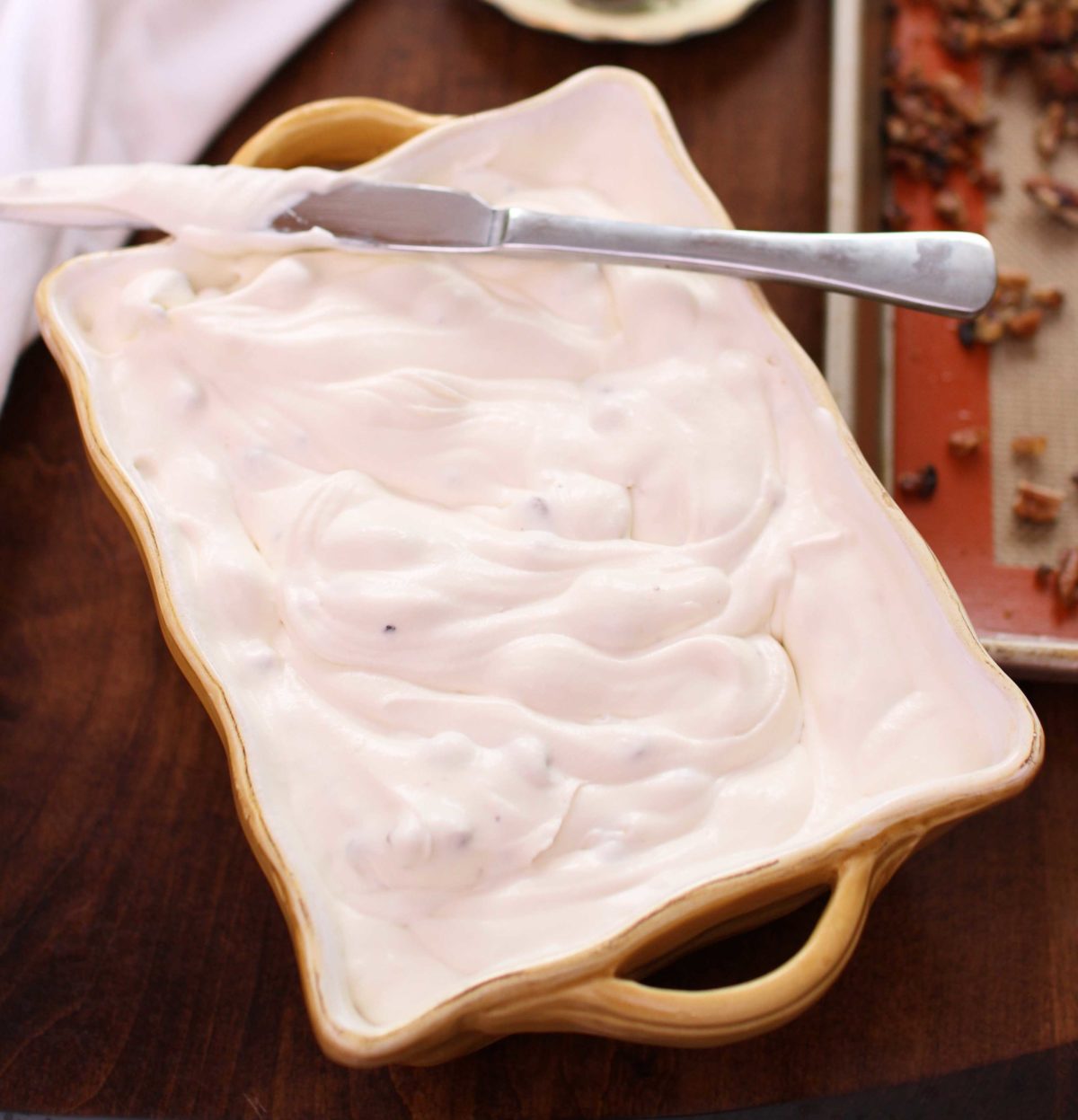 butter pecan ice cream in a yellow long baking dish with a knife resting on the side of the dish.