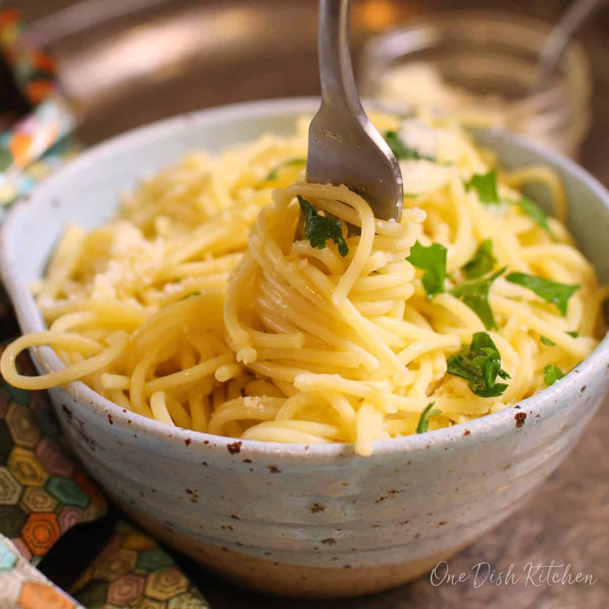 a single serving of buttered noodles with parmesan cheese in a bowl with a fork on the side.