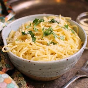 a single serving of buttered noodles with parmesan in a bowl topped with fresh parsley.