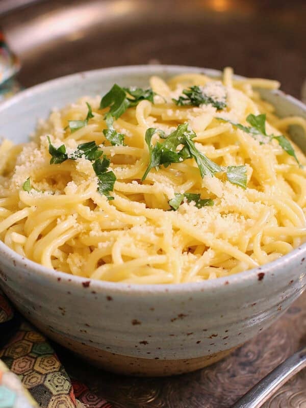 a single serving of buttered noodles with parmesan in a bowl topped with fresh parsley.