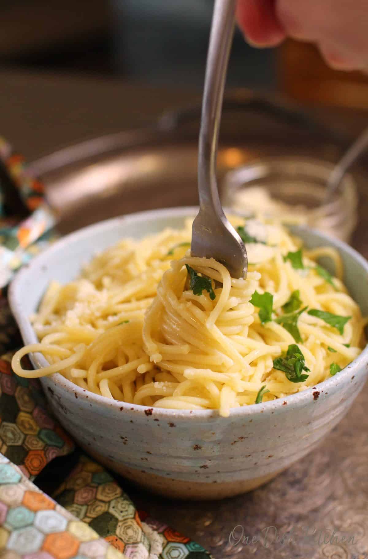 Pasta twirled on a fork from a bowl of pasta topped with parmesan cheese and chopped parsley.
