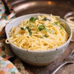 a blue bowl filled with buttered noodles topped with fresh parsley.