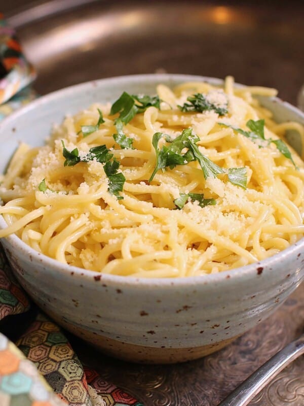a blue bowl filled with buttered noodles topped with fresh parsley.