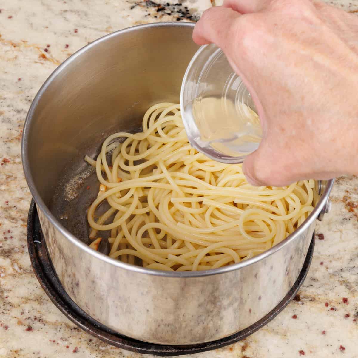 adding pasta water to cooked pasta in a pot.