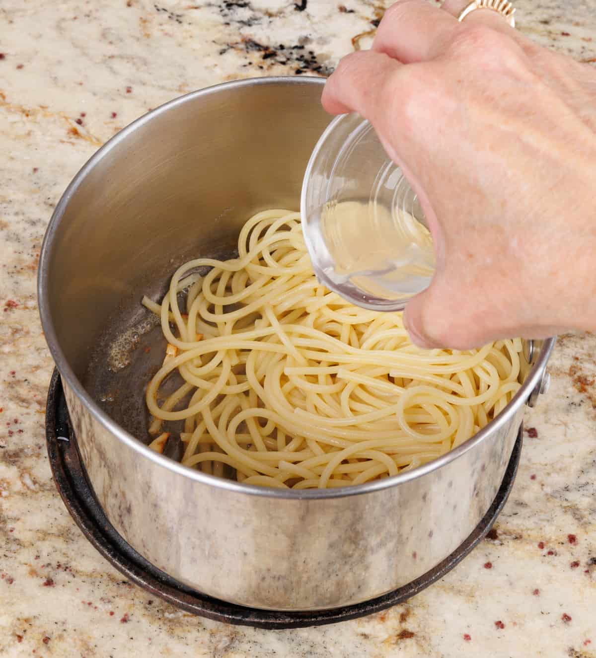 adding pasta water to cooked pasta in a pot.