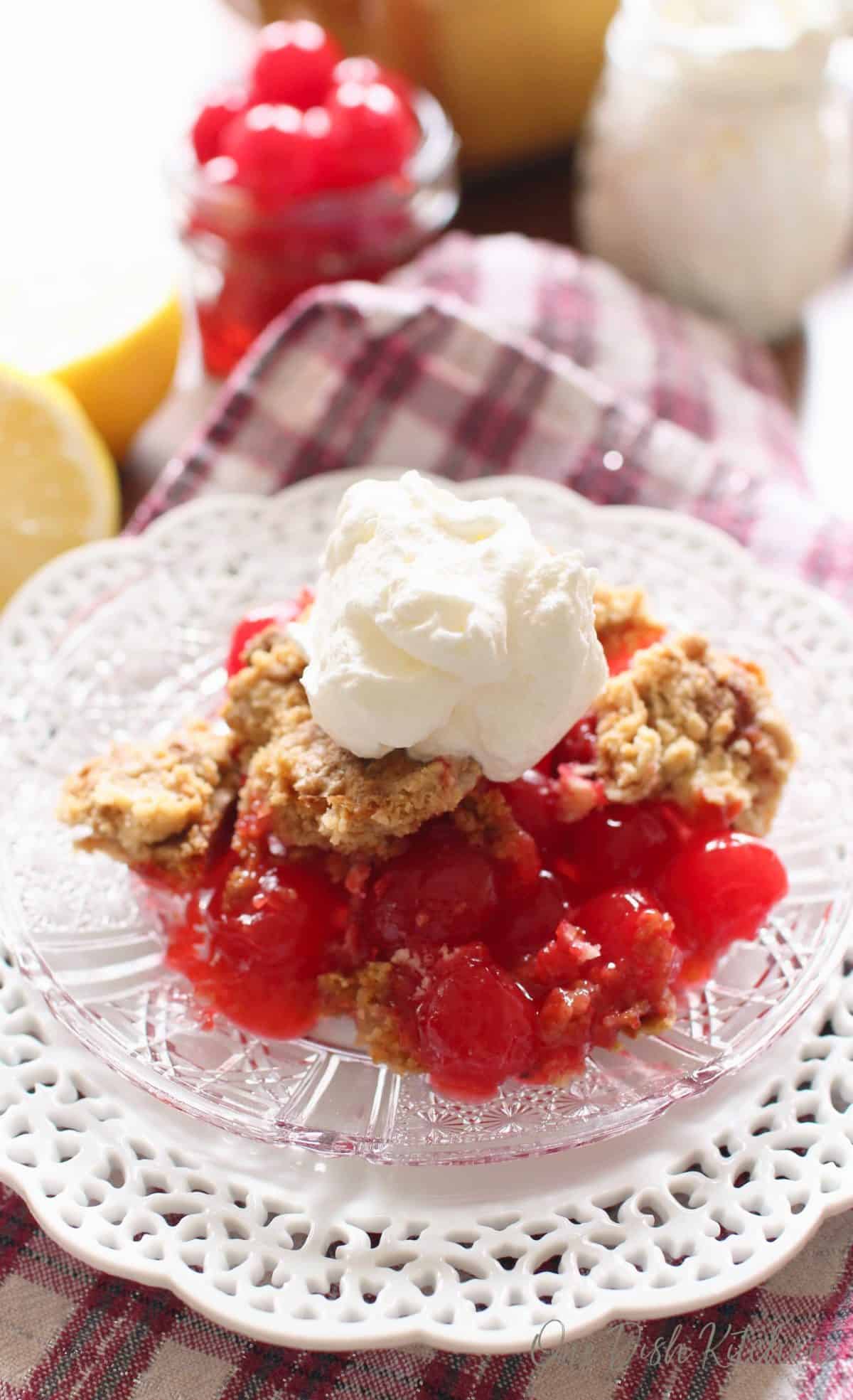 a cherry pie topped with whipped cream next to a bowl of cherries.