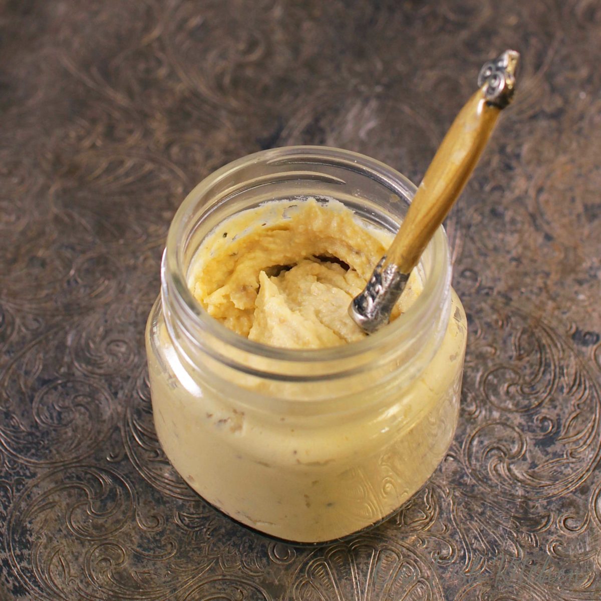 An overhead view of a jar of chickpea hummus with a gold spoon sticking out of the top.