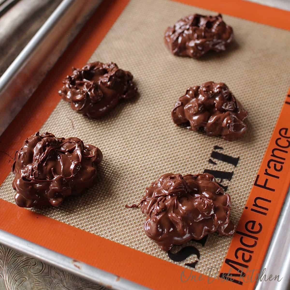 Melted chocolate mixture on a lined baking sheet making five candies.