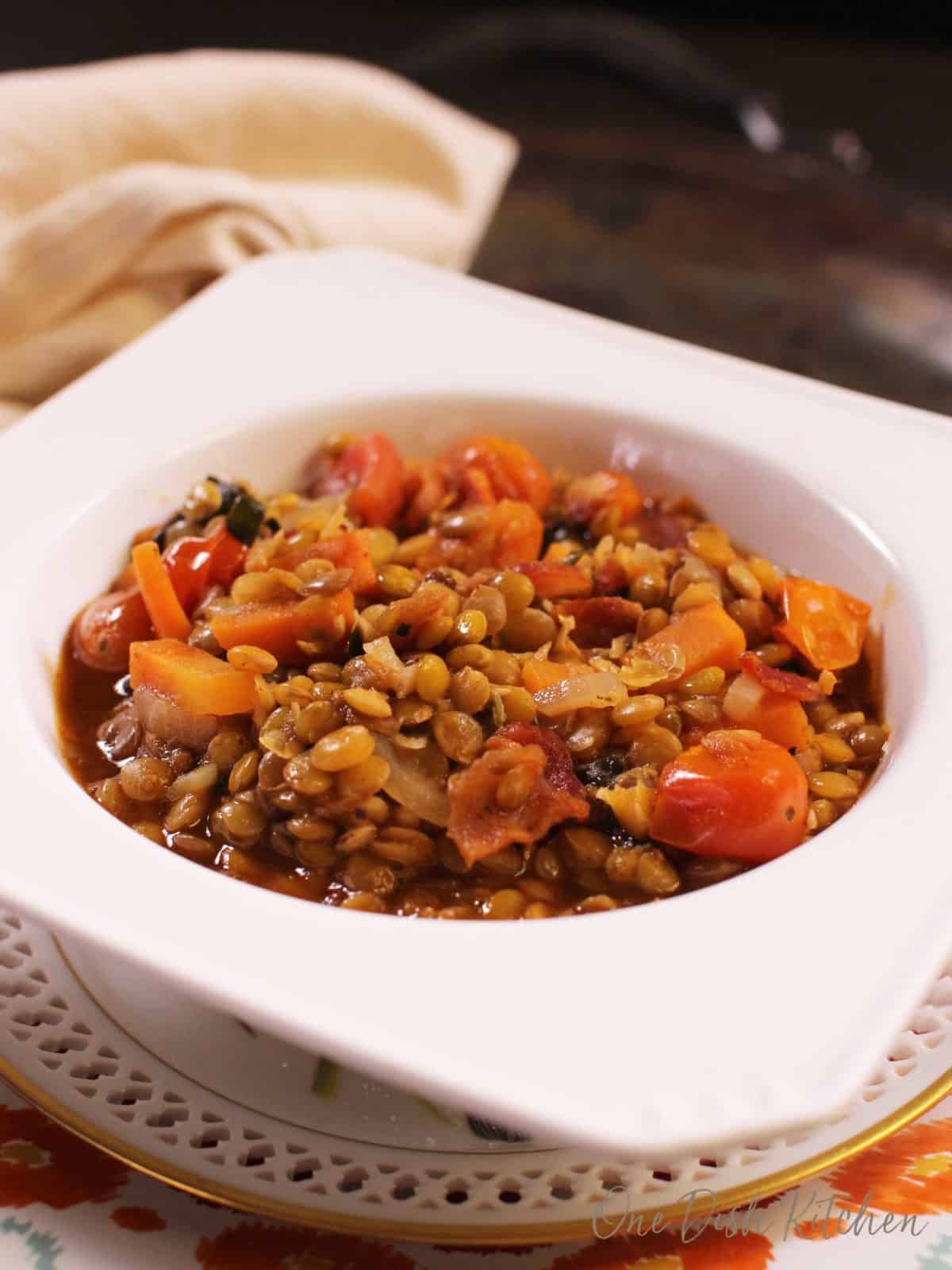 A bowl of lentil stew topped with bits of bacon and chopped tomatoes. 